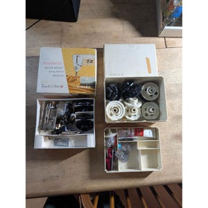 May include: A collection of Singer sewing machine accessories including a box labelled Accessories Deluxe Zig-Zag Sewing Machine Model 620 Touch & Sew, a box of white and black bobbins, and a box containing various metal presser feet and small tools.