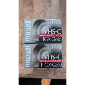 May include: Two Maxell VHS-C camcorder videocassette tapes. The boxes are gold with black and white text, including "VHS-C Premium High Grade HGX-Gold" and "TC-30 62 m". The tapes are for camcorders.