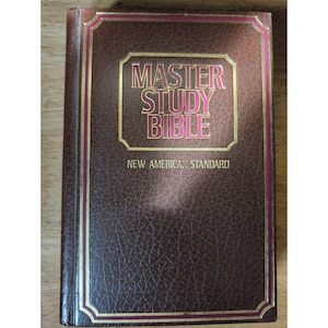 May include: A brown, textured hardcover book titled Master Study Bible New American Standard. The cover features gold-colored lettering and decorative border lines, with a rectangular frame surrounding the main title text on the front.