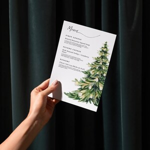 May include: A white menu card with the word "Menu" at the top. The card features a watercolour illustration of a Christmas tree. The menu lists a three-course meal: Roasted Butternut Squash Soup, Herb-Roasted Turkey + Cranberry Sauce, and Classic Yule Log.