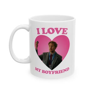 May include: White ceramic mug with the text "I LOVE MY BOYFRIEND" in pink. The mug features a pink heart with a photo of a man inside. The mug has a white handle.