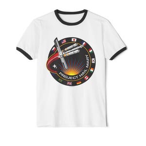 May include: White t-shirt with black trim featuring a circular graphic with a spaceship design, flags, and the text "PROJECT HAIL MARY". The graphic includes the flags of several countries.