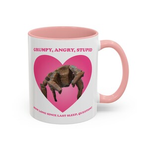 May include: White ceramic mug with a pink interior and handle. The mug features a pink heart with a brown insect illustration. Text on the mug reads "GRUMPY, ANGRY, STUPID" and "HOW LONG SINCE LAST SLEEP, QUESTION?"