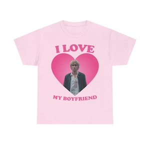 May include: A light pink t-shirt with the text "I LOVE" above a pink heart containing a photo of a person. Below the heart, the text reads "MY BOYFRIEND". The t-shirt is a crew neck style.