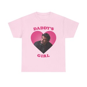 Peut inclure: T-shirt rose avec un graphique en forme de cœur représentant le visage d'un homme et le texte "DADDY'S GIRL" en rose.