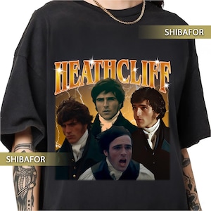 Könnte beinhalten: Schwarzes T-Shirt mit einem Retro-Grafikdesign, das vier Männer und das Wort "HEATHCLIFF" in Gold zeigt. Das Design hat eine Vintage-Ästhetik mit Blitzeffekten.