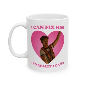 May include: White ceramic mug featuring the text "I CAN FIX HIM" in pink, with a pink heart containing a man in a work vest. The text "(NO REALLY I CAN!)" is below the heart.