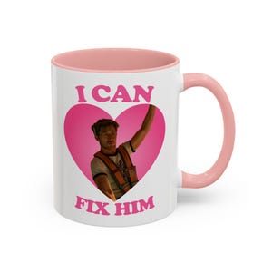 May include: White ceramic mug with a pink interior and handle. The mug features a pink heart with a man inside and the text "I CAN FIX HIM" in pink. A fun and quirky gift idea.