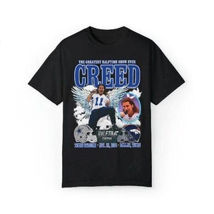 May include: Black t-shirt with a vintage-style graphic featuring the band Creed. The graphic includes the band's name, a photo of the lead singer, and the text "The Greatest Halftime Show Ever".