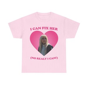 Può includere: Una t-shirt a maniche corte rosa chiaro con una grande grafica a forma di cuore rosa scuro sul petto. All'interno del cuore c'è la fotografia di una persona con i capelli biondi. Il testo I CAN FIX HER e (NO REALY I CAN!) è in rosa scuro.