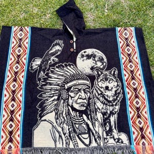 May include: Black hooded poncho with Native American design. Features an eagle, wolf, full moon, and a Native American chief. The sides have a colorful geometric pattern. The bottom has a fringe.