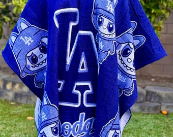 Op de afbeelding: Een blauwe poncho met het logo van de Los Angeles Dodgers en cartoonfiguren. De poncho heeft een capuchon en een knoopsluiting bij de hals. Het ontwerp bevat de letters "LA" en het woord "Dodgers" in wit.