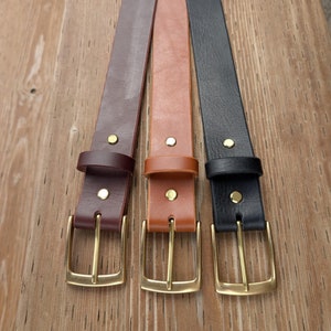 May include: Three leather belts in dark brown, tan, and black. Each belt features a smooth finish, a matching leather keeper loop, two gold-toned metal rivets, and a rectangular gold-toned metal buckle with a single prong for secure fastening.