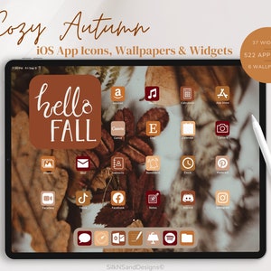 Puede incluir: Una pantalla de tableta digital que muestra una colección de iconos de aplicaciones marrones y rojos con un tema otoñal. Los iconos están dispuestos en una cuadrícula y incluyen aplicaciones como Amazon, Canva, Facebook, Instagram y más. La pantalla también presenta un icono cuadrado grande de color marrón con el texto "hello FALL" en blanco. La tableta está sobre una superficie blanca con un bolígrafo de punta blanca a su lado. El texto "Cozy Autumn" se muestra encima de la tableta, junto con el texto "iOS App Icons, Wallpapers & Widgets". El texto "37 Widgets, 522 App Icons, 6 Wallpapers" se muestra en la esquina superior derecha de la imagen.