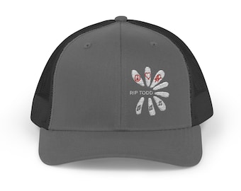 May include: A gray trucker hat with a black mesh back. The front of the hat features a white embroidered design of a flower with peace symbols, hearts, and musical notes. The text "RIP TODD" is below the flower.