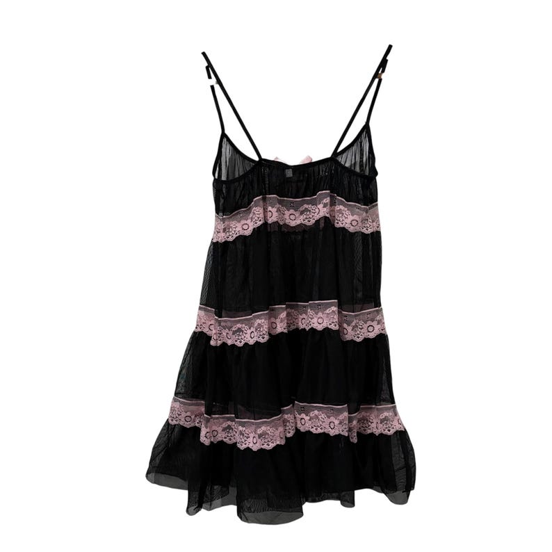 May include: Black lingerie slip with spaghetti straps and a tiered design. The slip features pink lace trim and a small bow detail at the neckline. The sheer fabric creates a delicate and feminine look.