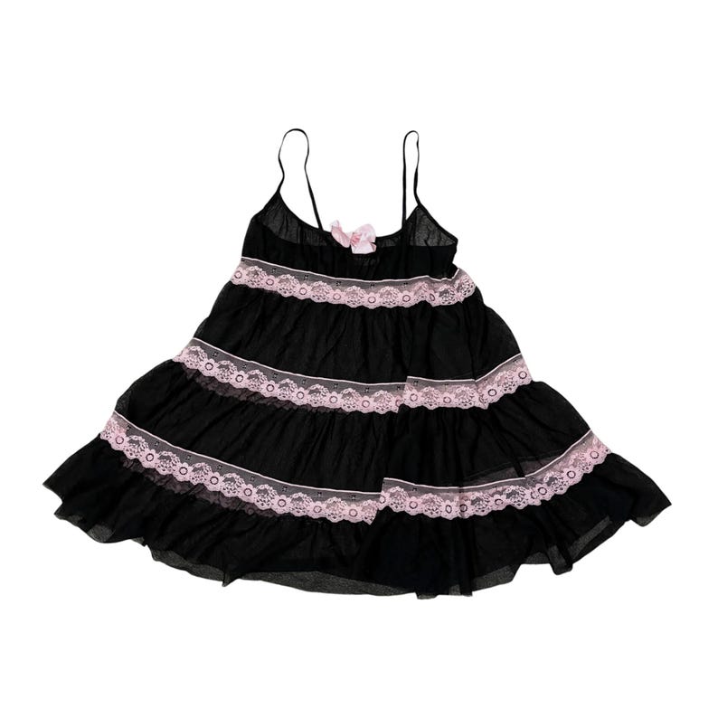 May include: Black babydoll dress with spaghetti straps and a tiered skirt. The dress features pink lace trim and a small pink bow at the bust. The lightweight fabric creates a flowing silhouette.