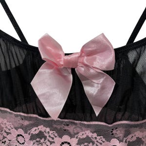 May include: Black lingerie top with a pink satin bow and spaghetti straps. The top features a pink lace trim along the bottom edge. The fabric appears to be a sheer mesh material.