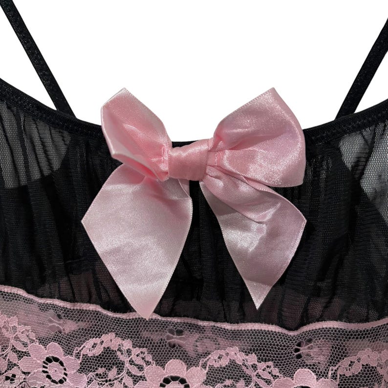May include: Black lingerie top with a pink satin bow and spaghetti straps. The top features a pink lace trim along the bottom edge. The fabric appears to be a sheer mesh material.