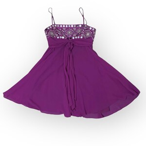 May include: A vibrant purple dress with spaghetti straps and a flowing skirt. The bodice is embellished with silver sequins and beads, and a matching tie cinches the waist. The dress is designed for a formal occasion.