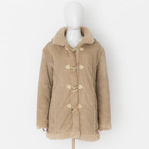 May include: A tan-colored coat with a shearling collar and lining. The coat features toggle closures and a longline silhouette. The coat is displayed on a mannequin against a white background. The coat is a winter outerwear garment.