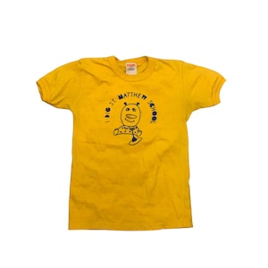 May include: A yellow t-shirt with a blue graphic of a cartoon character and the text "I DIG ST. MATTHEW SCHOOL".