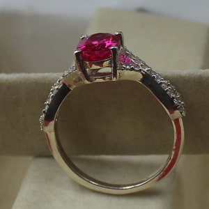 May include: A gold ring with a large, oval-cut, bright pink gemstone. The band is embellished with smaller, clear gemstones. The ring's design is showcased against a neutral backdrop. The ring's design is highlighted against a neutral backdrop.