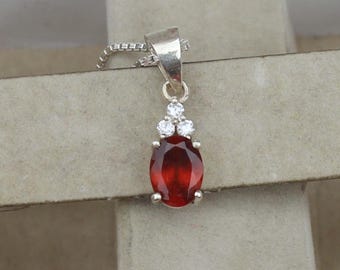 May include: A silver pendant with a deep red oval gemstone and three smaller white gemstones above it. The pendant hangs from a delicate silver chain, showcasing a classic and elegant design.