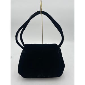 May include: A small, black velvet handbag with a rectangular body and a curved handle. The bag has a flap closure and a soft, plush texture. The handle is also made of black velvet.