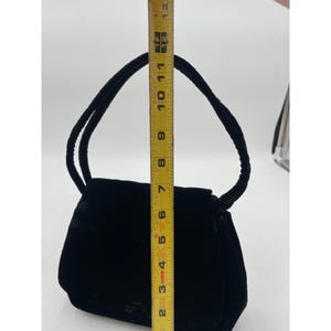 May include: A black velvet handbag with a rounded rectangular shape and a top handle. The bag is approximately 7 inches tall and 9 inches wide. The handle is made of the same velvet material as the bag.