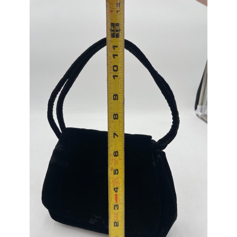 May include: A black velvet handbag with a rounded rectangular shape and a top handle. The bag is approximately 7 inches tall and 9 inches wide. The handle is made of the same velvet material as the bag.