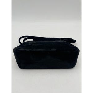 May include: A black velvet handbag with a rectangular shape and a short handle. The bag has a soft, textured appearance and a simple, elegant design. The handle is also made of black velvet.