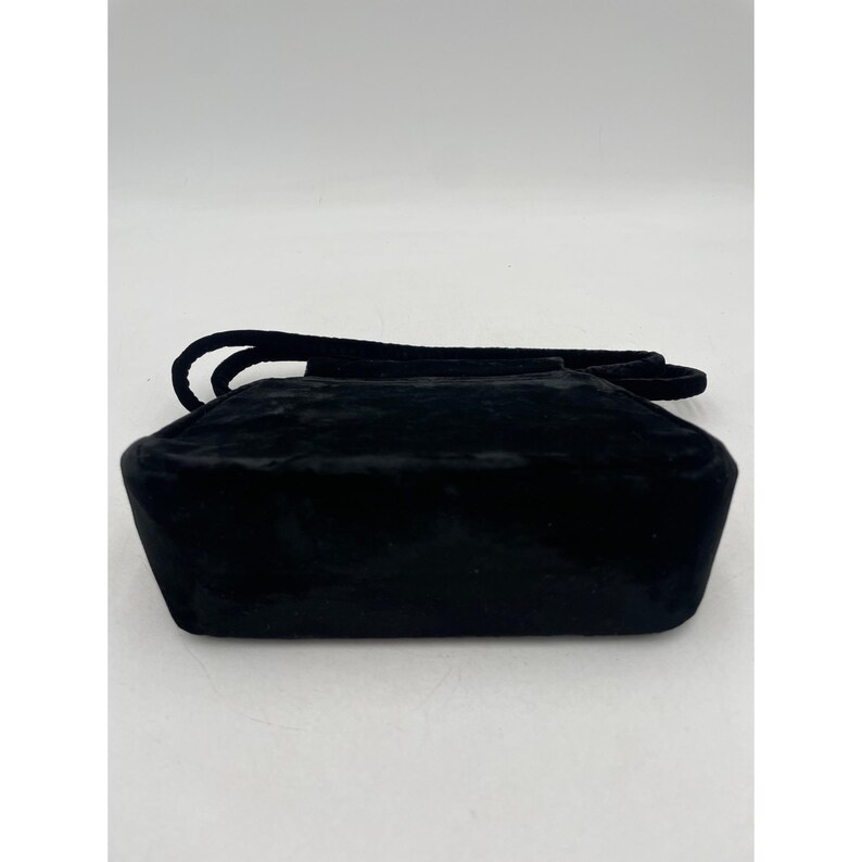 May include: A black velvet handbag with a rectangular shape and a short handle. The bag has a soft, textured appearance and a simple, elegant design. The handle is also made of black velvet.
