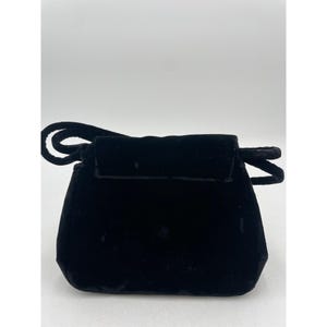May include: A small, black velvet handbag with a rounded bottom and a flap closure. The bag has a short handle and a loop detail on the top. The velvet material gives the bag a soft, luxurious appearance.