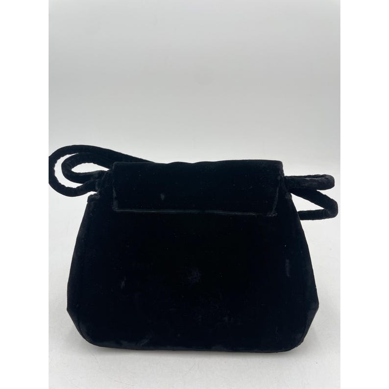 May include: A small, black velvet handbag with a rounded bottom and a flap closure. The bag has a short handle and a loop detail on the top. The velvet material gives the bag a soft, luxurious appearance.