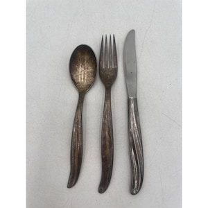 May include: A set of vintage silverware including a spoon, fork, and knife. The spoon has an oval bowl, the fork has four tines, and the knife has a curved blade. All pieces have a silver finish with a curved handle design.