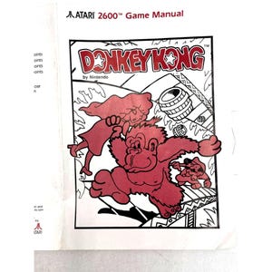 May include: An Atari 2600 Game Manual for Donkey Kong by Nintendo. The cover features a red and black illustration of a gorilla holding a figure, with barrels rolling down a structure. The text reads Atari 2600 Game Manual and Donkey Kong.