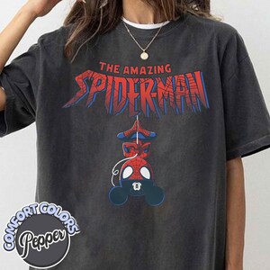 Pu&ograve; includere: T-shirt grigio scuro con la scritta "THE AMAZING SPIDER-MAN" in rosso e blu. Sotto, un disegno a cartoni animati di Spider-Man. La maglietta ha un logo Comfort Colors e Pepper.