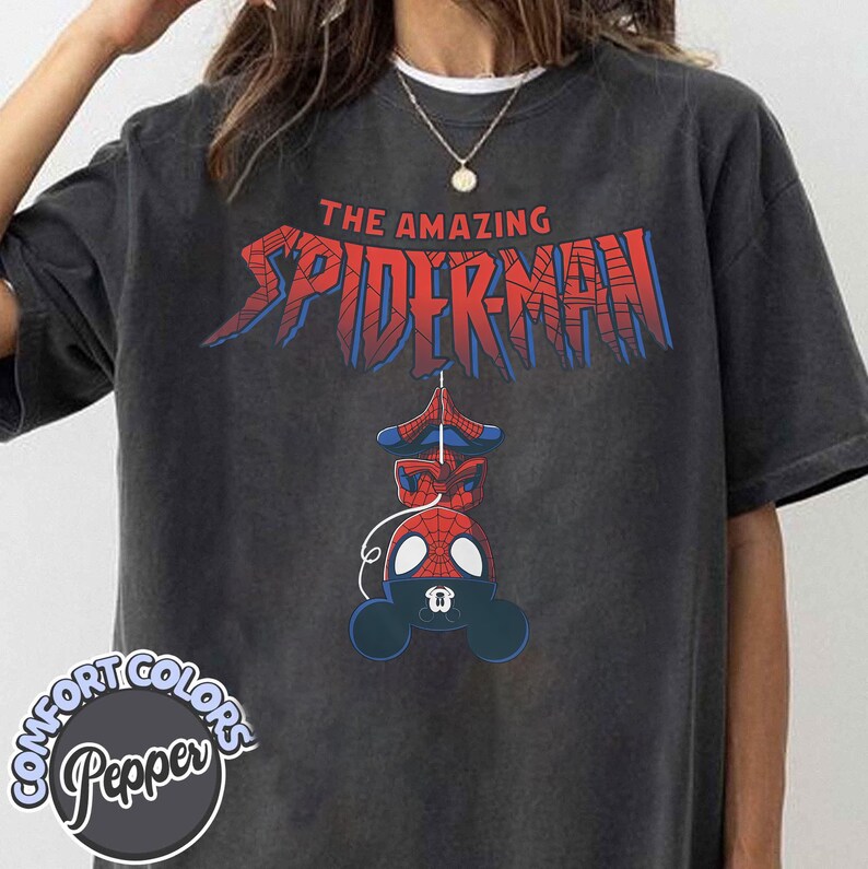 Pu&ograve; includere: T-shirt grigio scuro con la scritta "THE AMAZING SPIDER-MAN" in rosso e blu. Sotto, un disegno a cartoni animati di Spider-Man. La maglietta ha un logo Comfort Colors e Pepper.