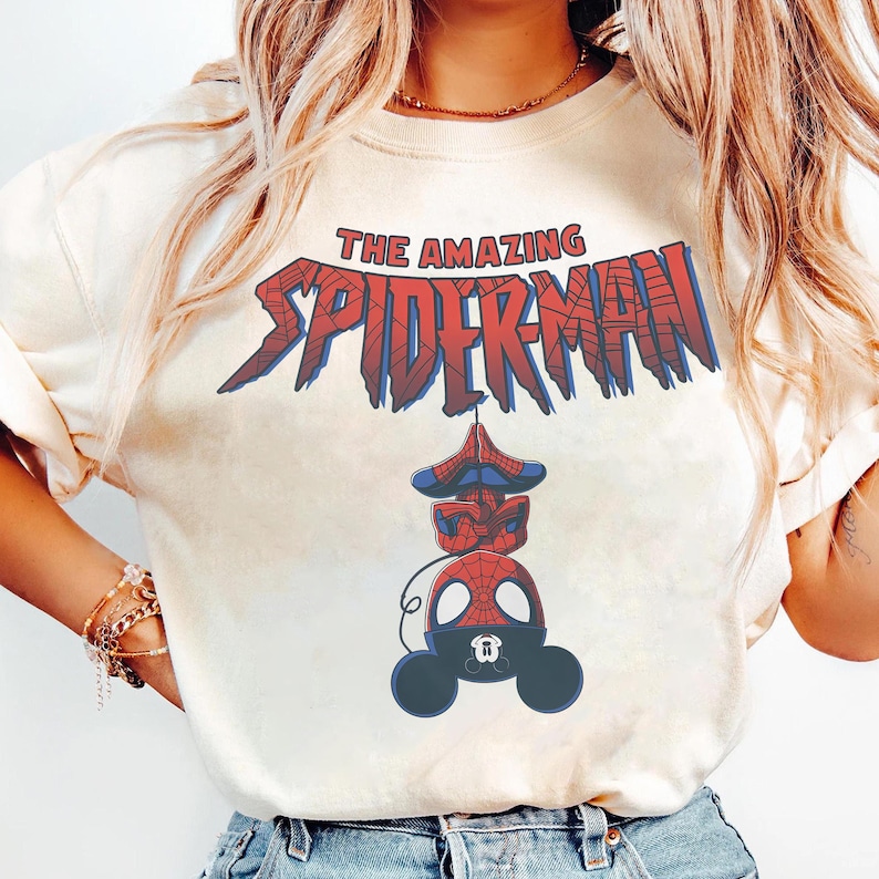 Pu&ograve; includere: T-shirt color crema con la scritta "THE AMAZING SPIDER-MAN" in rosso e blu. Sotto, una grafica della testa e del corpo di Spider-Man, disegnata nello stile di Mickey Mouse. La maglietta ha un girocollo e maniche corte.