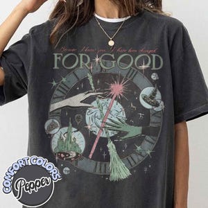 May include: Dark gray Comfort Colors t-shirt with a whimsical design featuring a clock face, hands, a wand, and the words "FOR GOOD." The design includes a castle, a witch's hat, and a broom. The text "Because I knew you, I have been changed" is above the main text.