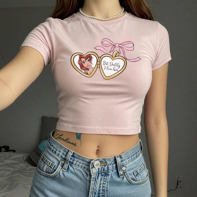Puede incluir: Camiseta rosa de manga corta y corte corto con una imagen de dibujos animados de una mujer en un medall&oacute;n con el texto "But, Dudley, I love him".