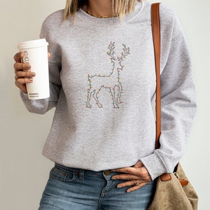 May include: A gray sweatshirt with a reindeer design made of Christmas lights. The reindeer is outlined in black and the lights are in various colors, including red, green, blue, and yellow.