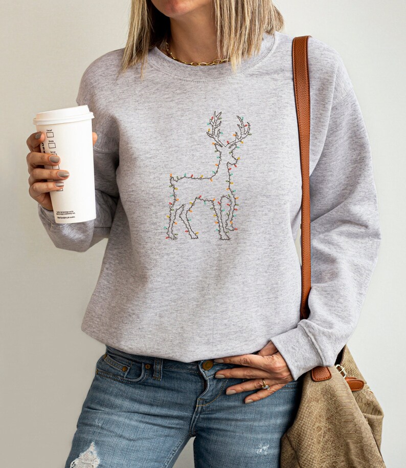 May include: A gray sweatshirt with a reindeer design made of Christmas lights. The reindeer is outlined in black and the lights are in various colors, including red, green, blue, and yellow.