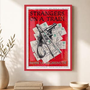 May include: A framed art print featuring a red background overlaid with black text from a book page. The title STRANGERS ON A TRAIN and author PATRICIA HIGHSMITH are printed in black. A detailed black and white illustration of a revolver is centered.