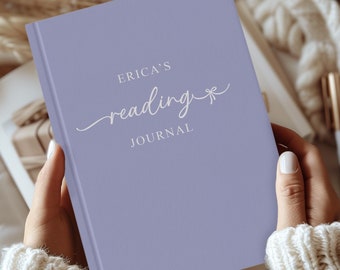 Puede incluir: Un diario de color lavanda con el texto "ERICA'S reading JOURNAL" en letras blancas. El diario tiene un pequeño lazo blanco en la portada.