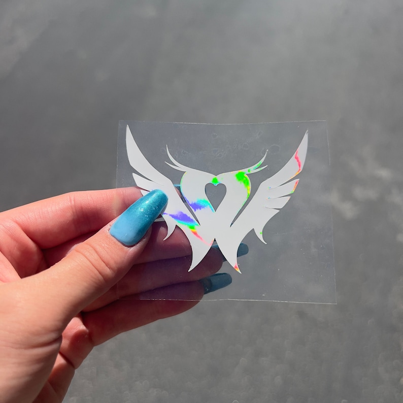 Puede incluir: Una pegatina de vinilo blanco con un dise&ntilde;o de coraz&oacute;n y alas. El coraz&oacute;n est&aacute; relleno de colores arco&iacute;ris iridiscentes.