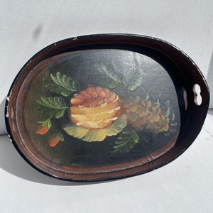 May include: Oval serving tray with a black background and a hand-painted floral design. The flowers are yellow, orange, and brown, with green leaves. The tray has a dark brown rim and cut-out handles.