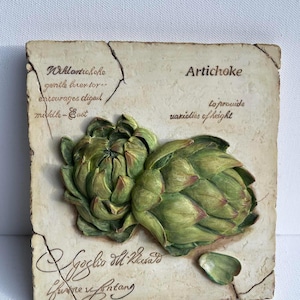 May include: A rectangular, off-white decorative plaque featuring two green artichokes in relief. The word "Artichoke" is printed on the plaque, along with other text. The plaque has a distressed, aged appearance with cracks.
