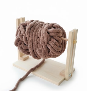 Può includere: Un rocchetto di legno con una grande palla di filato marrone. Il filato è spesso e strutturato, con un aspetto morbido e soffice. Il rocchetto è realizzato in legno chiaro e ha un design semplice e funzionale, ideale per progetti di maglia e uncinetto.